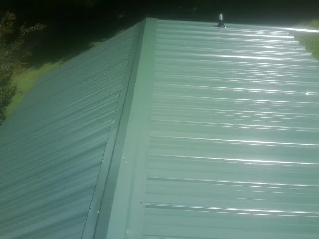 New green metal panels meeting at the ridge of a roof — Flat Roof Repair work by our crew in Glen Allen