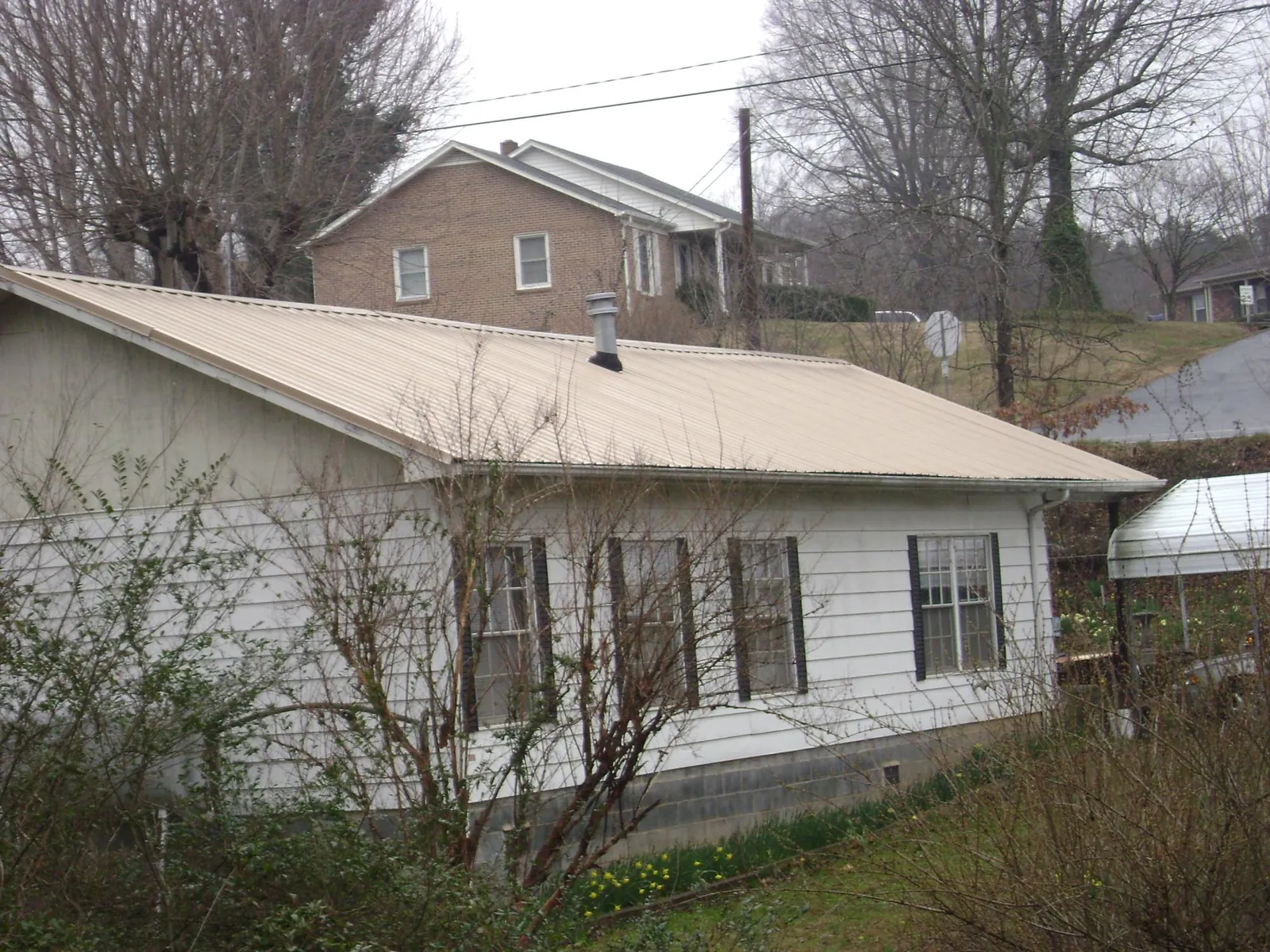 Tan metal roof on a white sided house set into a hillside — Commercial Roofing by Roofing Brothers in Glen Allen